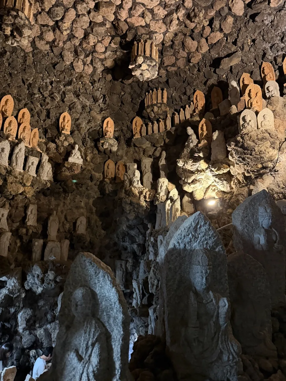 A dim cave lined floor-to-ceiling with carved stone Buddha statues