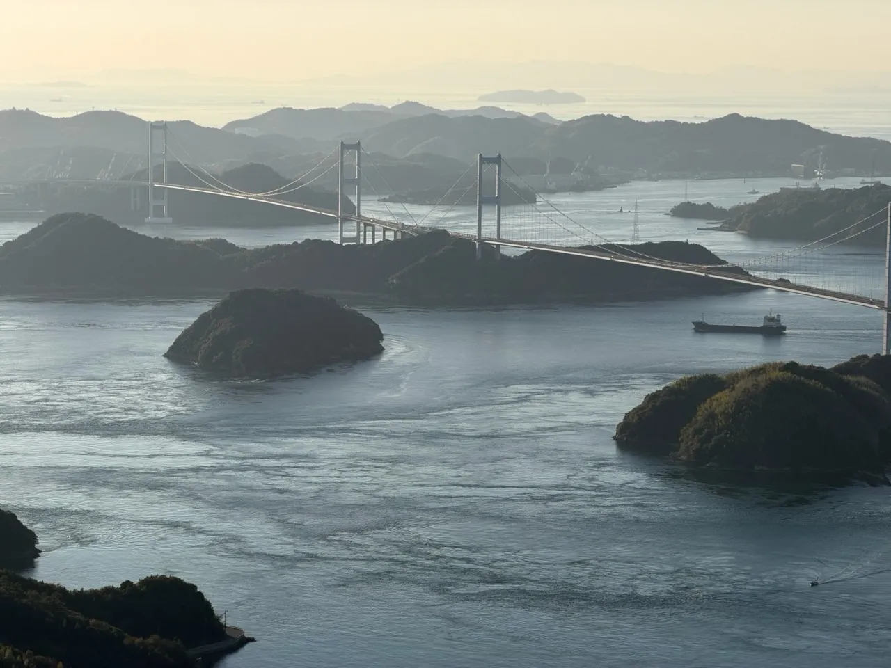 An elevated view of the long white Kurushima-Kaikyo triple suspension bridge crossing between islands in the Seto Inland Sea