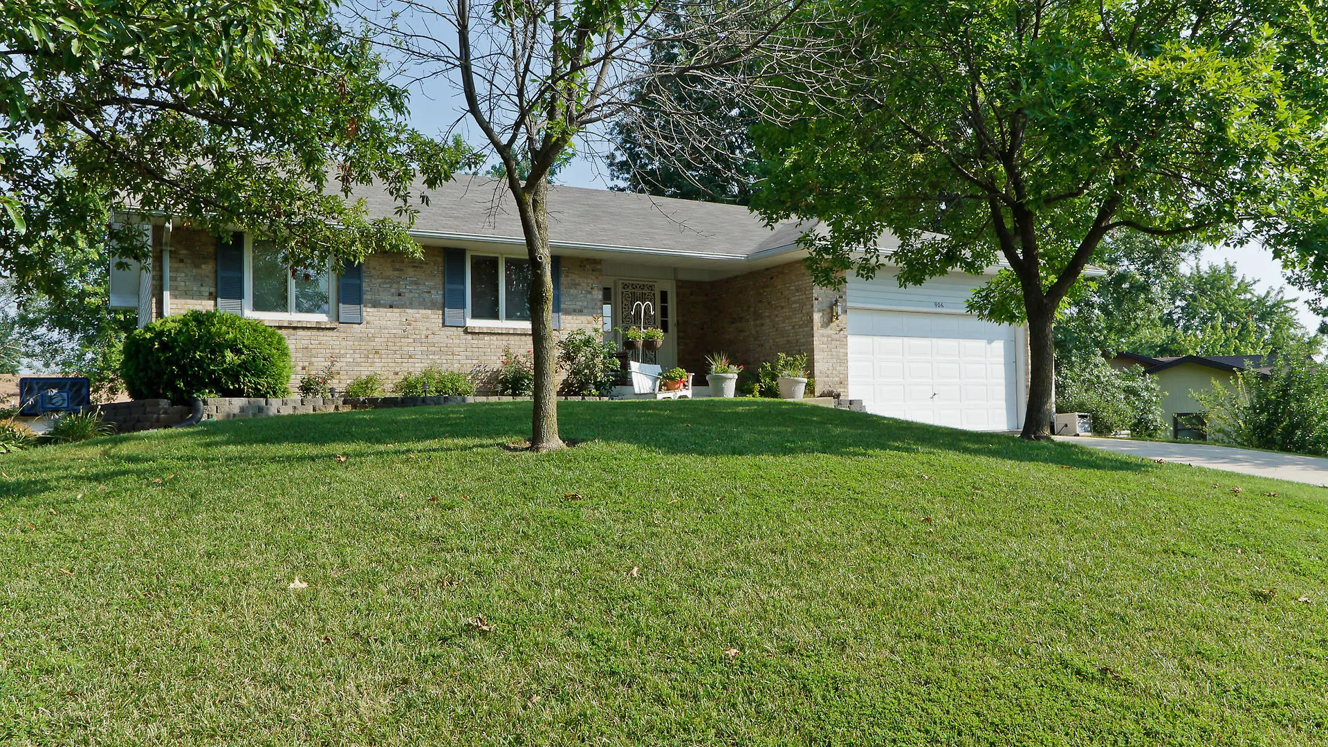 The house in 2012, a brick ranch with an attached two-car garage, framed by two large green trees in the front yard and a sloping lawn.