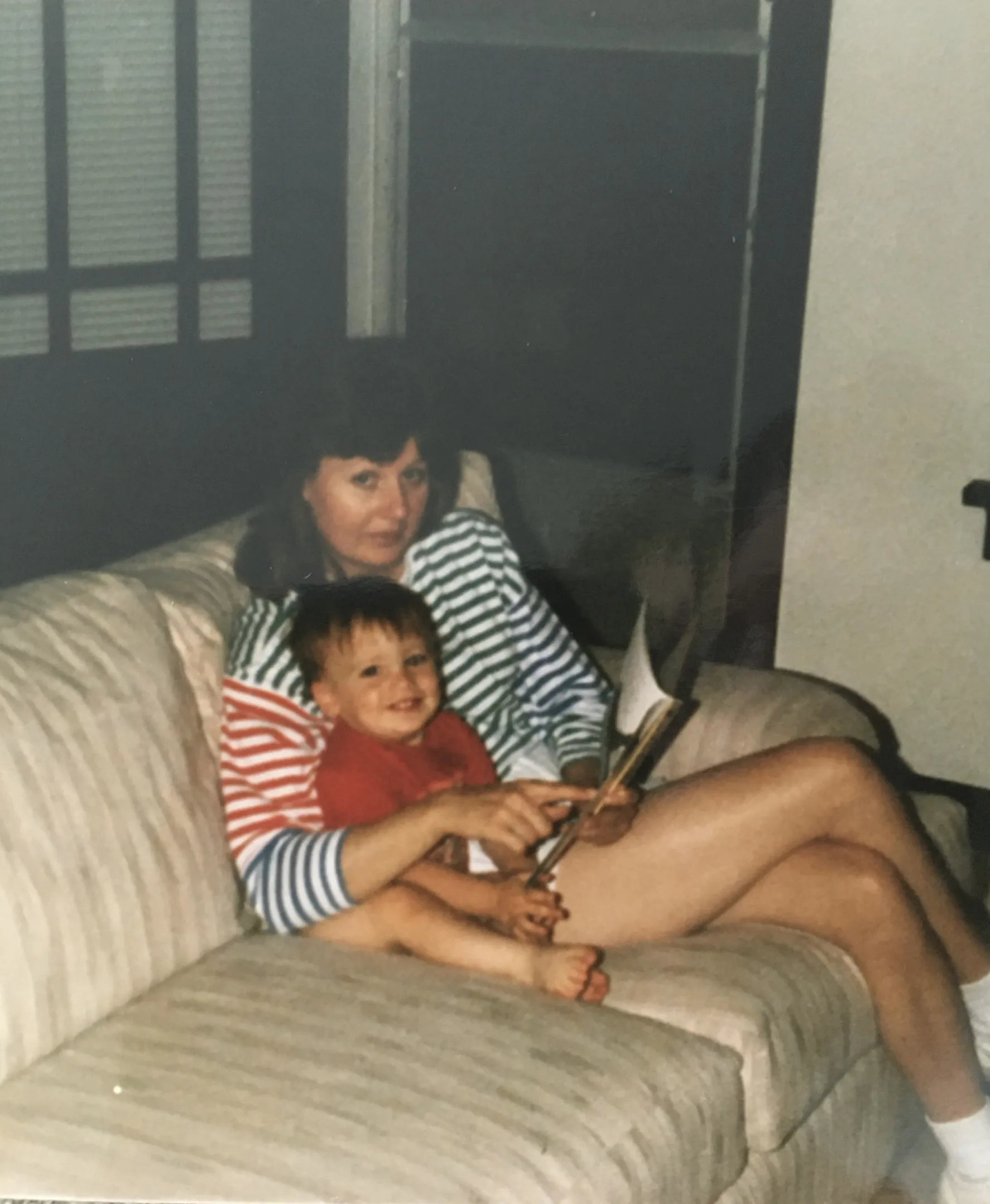 My mom reading to me on the couch as a toddler, me sitting in her lap in a little striped shirt
